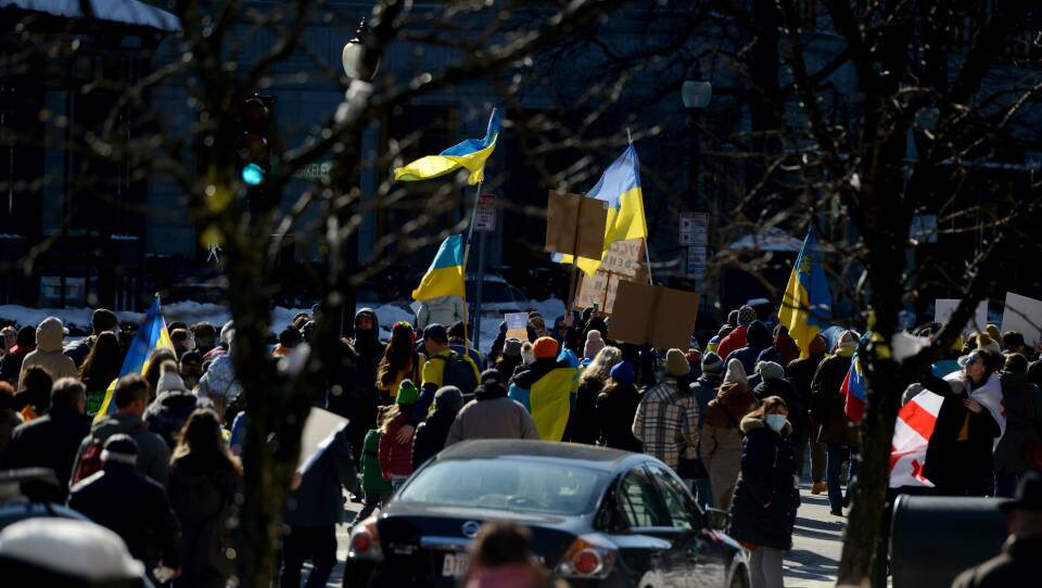 A crowd holding signs and flags marches down a street.