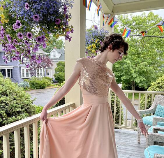 A young person wears a light pink sparkly dress, bracelets and a stylish headband.