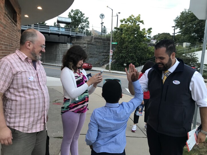 A man in a tie and vest high-fives a young child as two adults stand nearby.