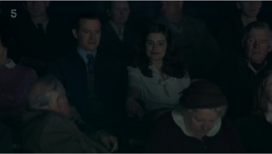 An older man turns around in a movie theater to yell at James