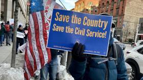 A protester holds up a blue sign with yellow letters reading "Save the civil service"