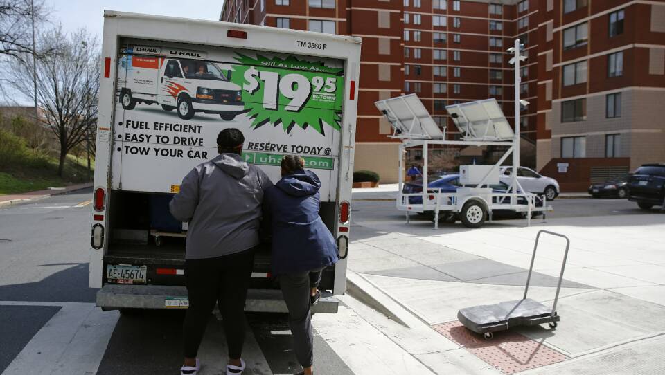Two people pull down the back door of a U-Haul truck outside a large apartment complex.