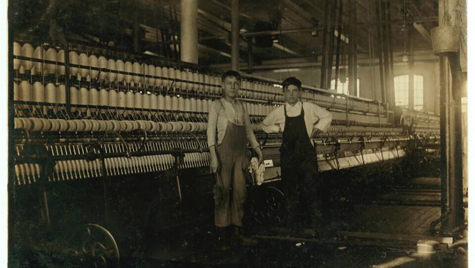 Two young children stand in a textile factory in this sepia photo
