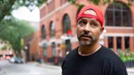 A man in a black T-shirt and backwards red baseball cap looks off camera on a gloomy day.