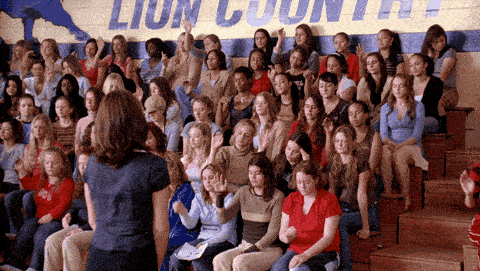 A large group of young women all raise their hands.