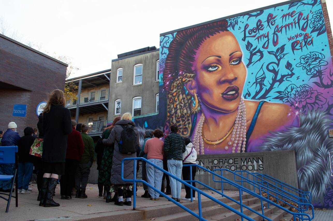 A brightly colored mural of a Black, transgender woman featuring the words "Look to me, my family. XOXO Rita"