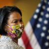 A woman wearing a floral face mask stands in front of a U.S. flag.