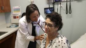 A doctor holds a patient's shoulder as she listens through a stethoscope to their lungs.