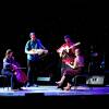 Four strings musicians play instruments under a spotlight on stage.