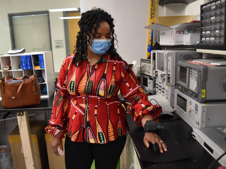 A Black woman rests her hand on a counter while wearing a medical device on her finger and wrist.