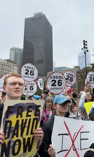 Individuals in a crowd hold a variety of signs, including one that says "Free David Now".