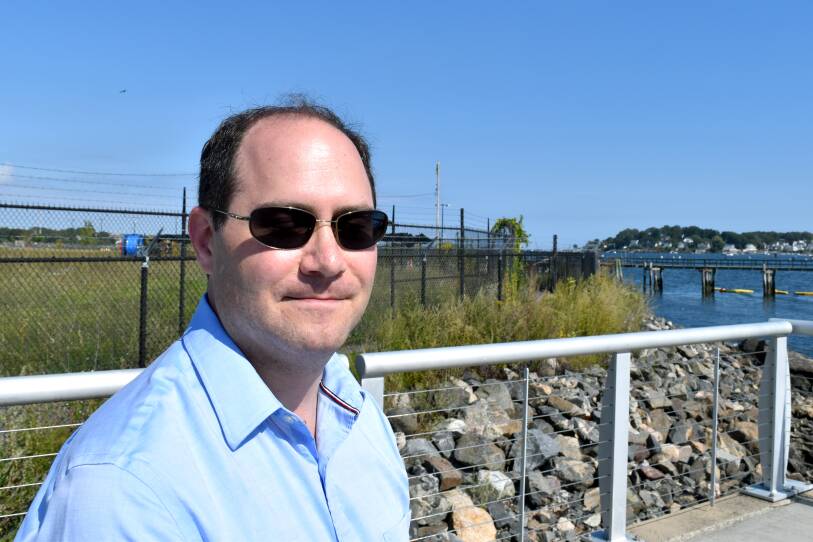 The mayor in sunglasses stands by the shore.