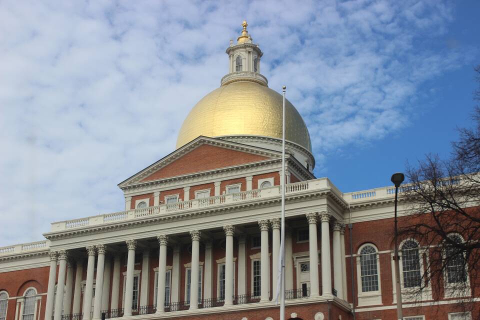 The gold dome of the Massachusetts State House shines under a partly cloudy sky on an early spring day.