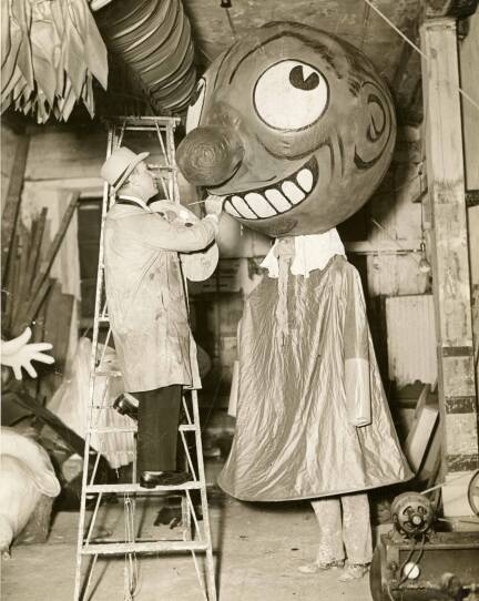 A man paints a cartoon-like face on a large balloon puppet.