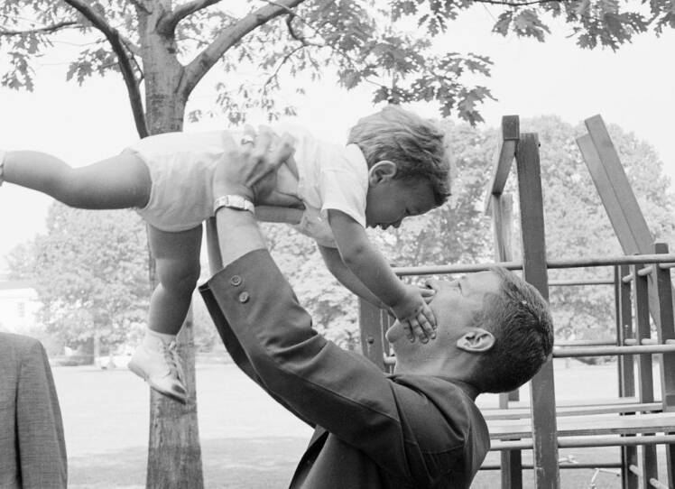 A black-and-white photo of a man in a suit lifting a toddler into the air.