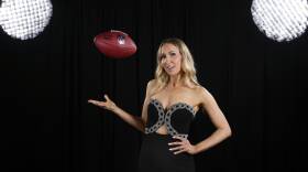 Nikki Glaser wears a black dress and bounces a football in the air with one hand.