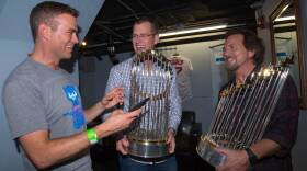 Two men hold World Series trophies as they talk to a third man.