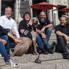 Five people sit next to a large gray dog sticking his tongue out on the steps of a museum.