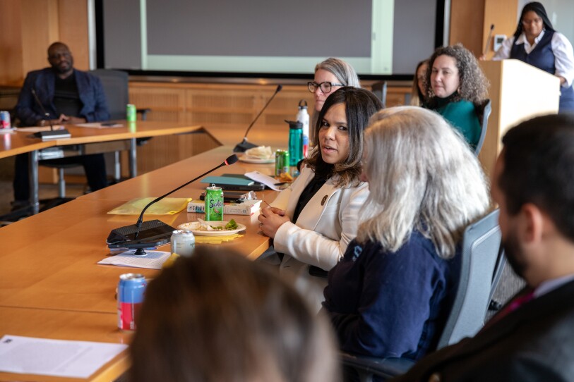 Woman sitting at a conference table with others turns to speak to the woman on her left as the group listens.