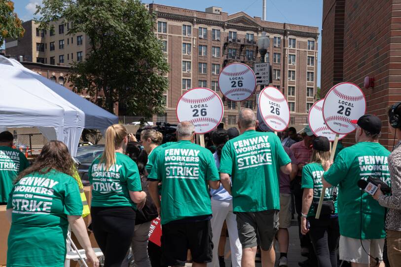 A group of people hold signs and wear green t-shirts that read "Fenway workers on Strike."