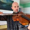 A man in a speckled gray turtleneck plays a viola, gazing away from the camera.