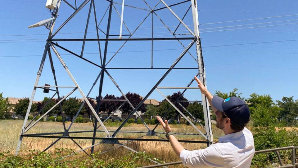 Jon Marmillo gestures at a box full of laser sensors on a transmission tower in Folsom, Calif. The sensors can read things like wind and temperature and give that data to utilities so they can safely transmit more power.