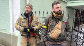 Two Ukrainian soldiers stand with guns outside a gate.