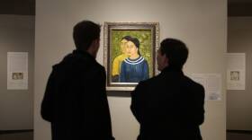 Two people stand and look at a well-lit oil painting