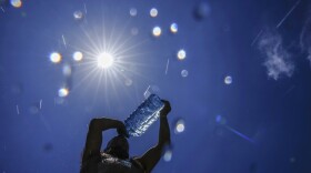 A silhouette of a person drinking from a large plastic bottle of water, illuminated by the bright sun.