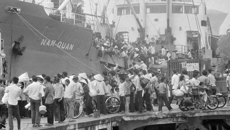 Hundreds of people try to get onto a massive steel boat in this black-and-white picture.
