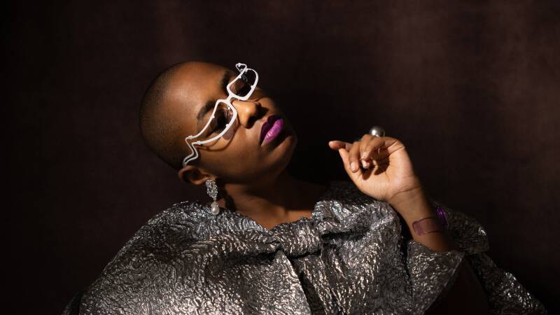 Cecile McLorin Salvant poses nonchalantly against a purple background, wearing a metallic cape.
