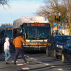 A city road with buses and cars. Two people cross the road.