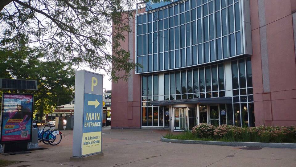A sign that says "main entrance St. Elizabeth's Medical Center" points toward a rotating glass door on one side of a large building.
