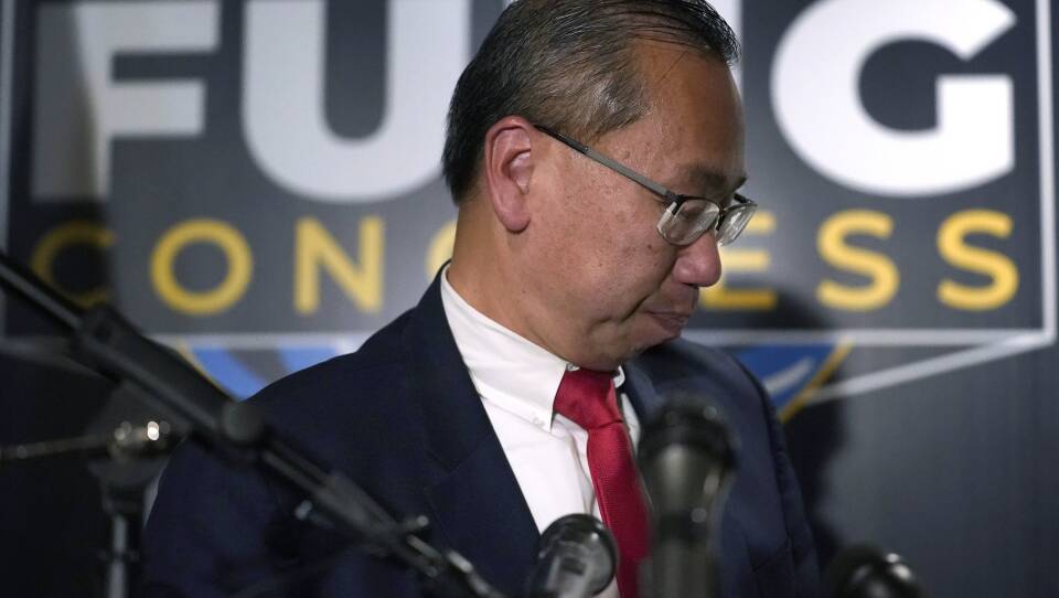 A man with glasses in a suit and tie steps back from several microphones, with pursed lips, as a FUNG CONGRESS sign hangs in the background.