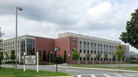 A school building with trees along the sidewalk outside. A sign says "DHS committed to academic and personal excellence!"