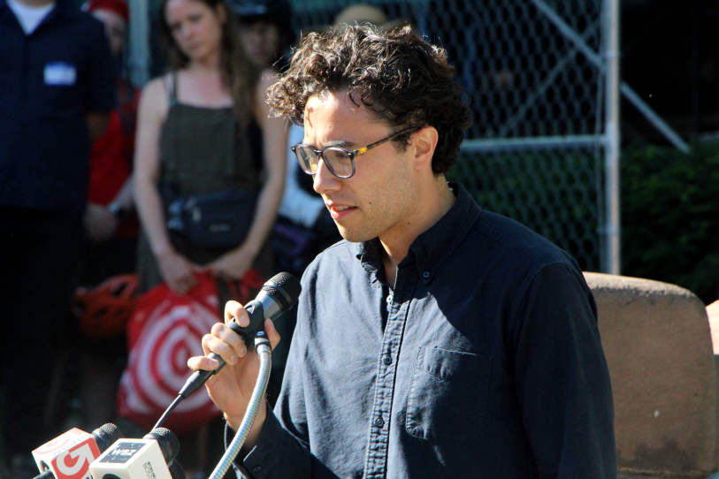 A young man in a buttondown looks downtrodden, gripping a microphone while he addresses a crowd.