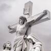 A white and gray photo of a crucifix atop a church depicts Christ on a cross with two figures below looking up in distress.