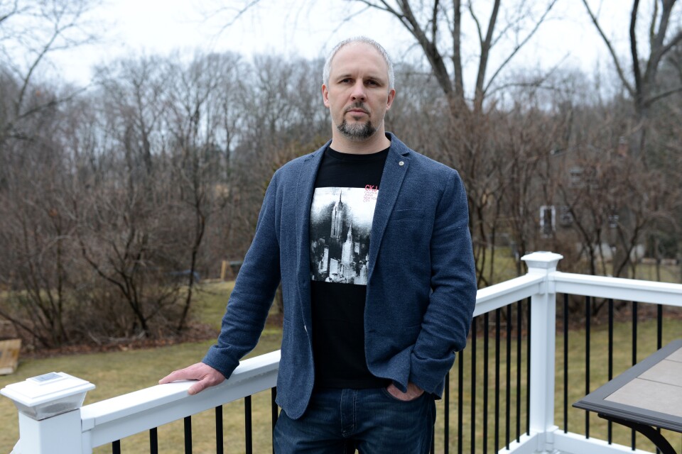 A man stands outside on a deck, his hand on the railing.