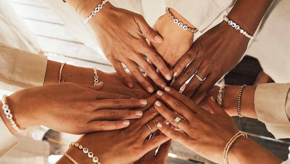 Nine hands reaching toward one another, with beaded bracelets on their wrists.
