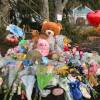 A memorial of flowers and stuffed animals in front of a blue house.