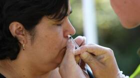 A person wearing gloves administers a nasal spray into a woman's nose.
