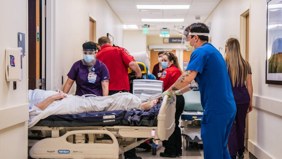 Several medical professionals wheel beds around a hallway.