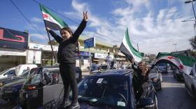 A kid waving a Syrian flag stands on the hood of a car