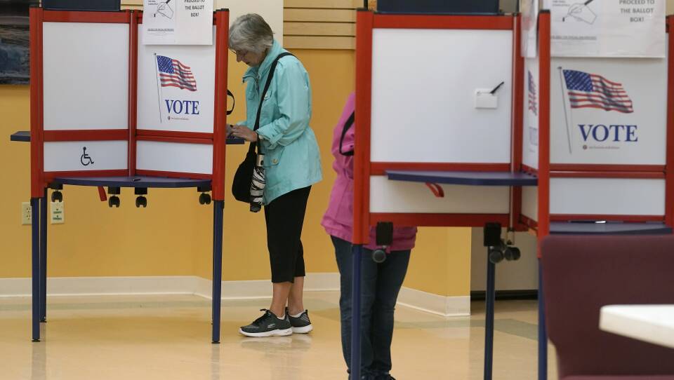 Two people in brightly colored rain jackets and sneakers separately vote, looking down at their ballots