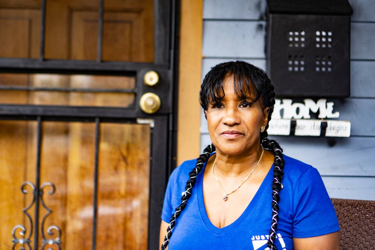 A woman in a blue T-shirt and long braids looks distantly off camera