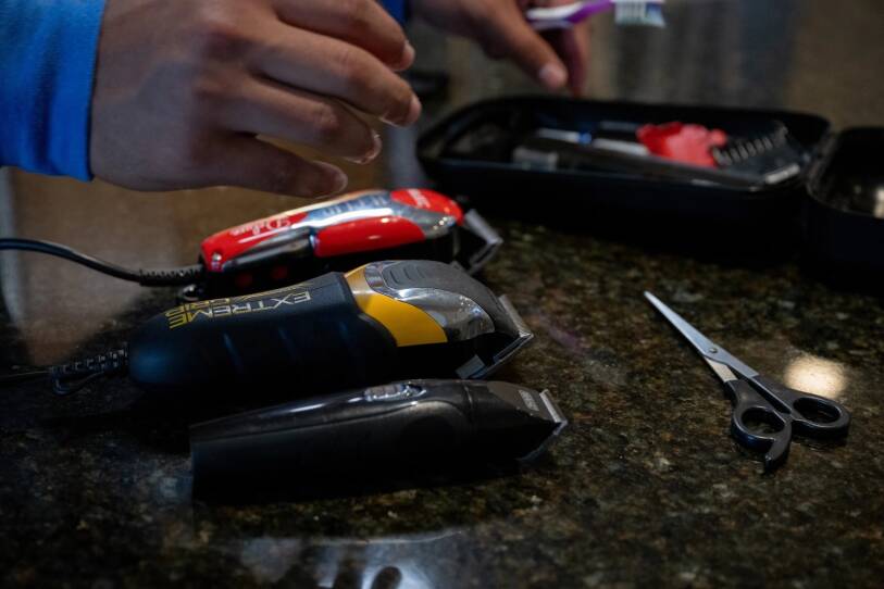 A close-up of a pair of hands reaching towards a collection of hair clippers and scissors on a counter.