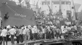 Hundreds of people try to get onto a massive steel boat in this black-and-white picture.