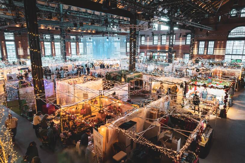 The SoWa open market, which is located in a huge industrial space, once a power generation plant. It's an overhead view of a grid of kiosks, which are all decorated with white, holiday lights. People are shopping.