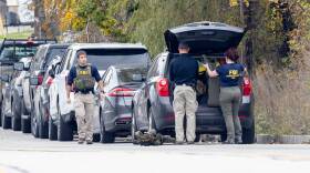 Three people affiliated with the FBI are milling around a car.