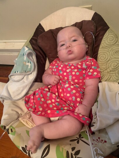 A baby dressed in a pink dress with an oxygen tube and feeding tube